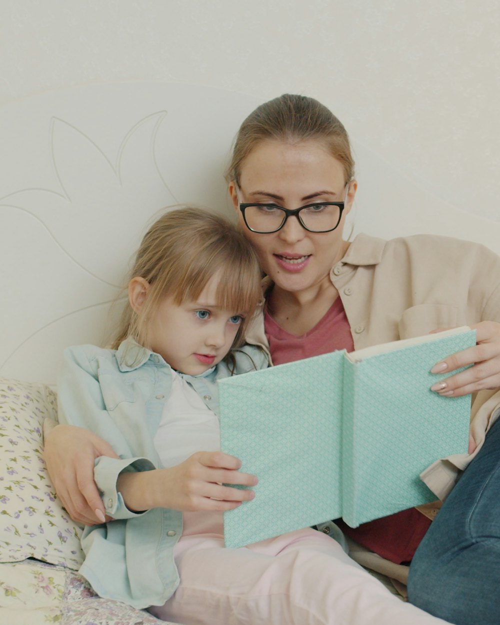 A mother reading a picture book with her daughter leaning into her.